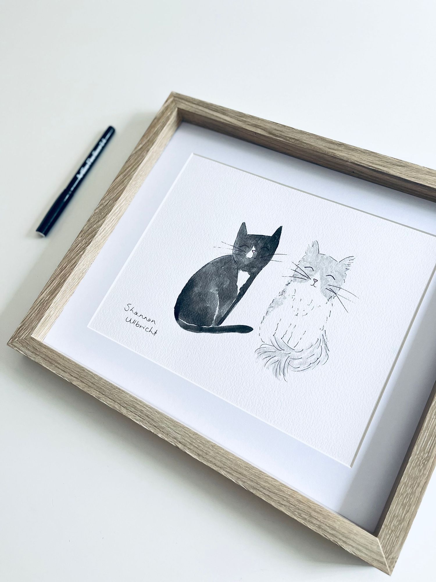 Hand painted illustration of two little cats sitting next to each other in a wooden frame.