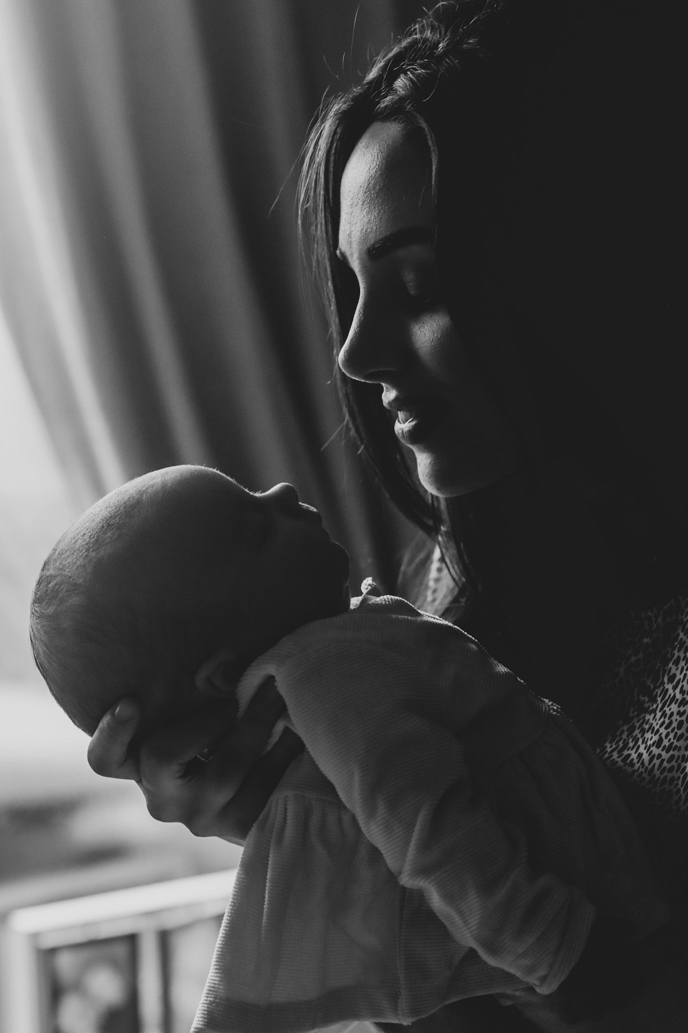 Artistic black and white portrait of mother holding baby in gentle lighting.
