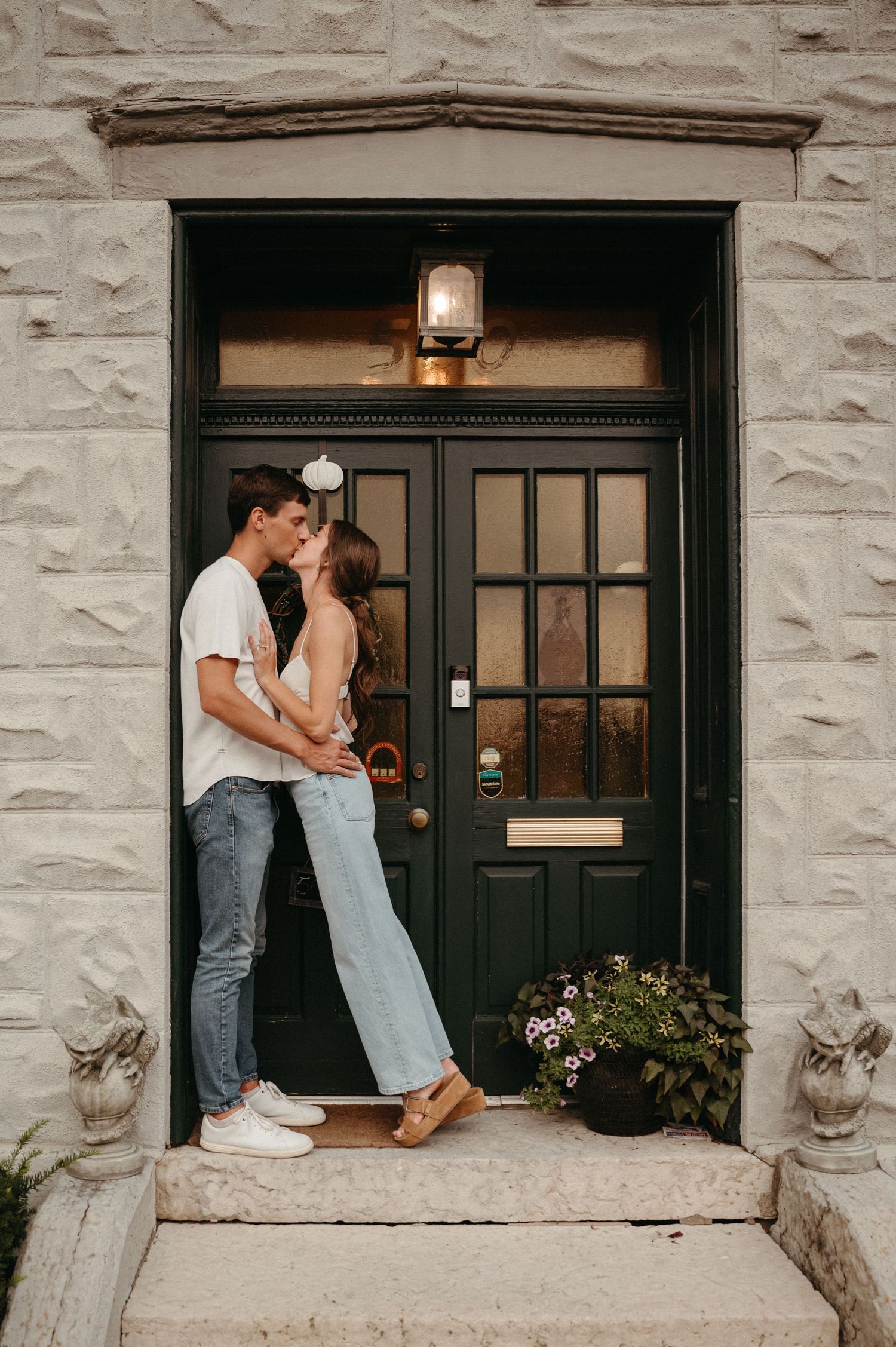 A couple sharing an intimate moment in a doorway of a stone building with black door.