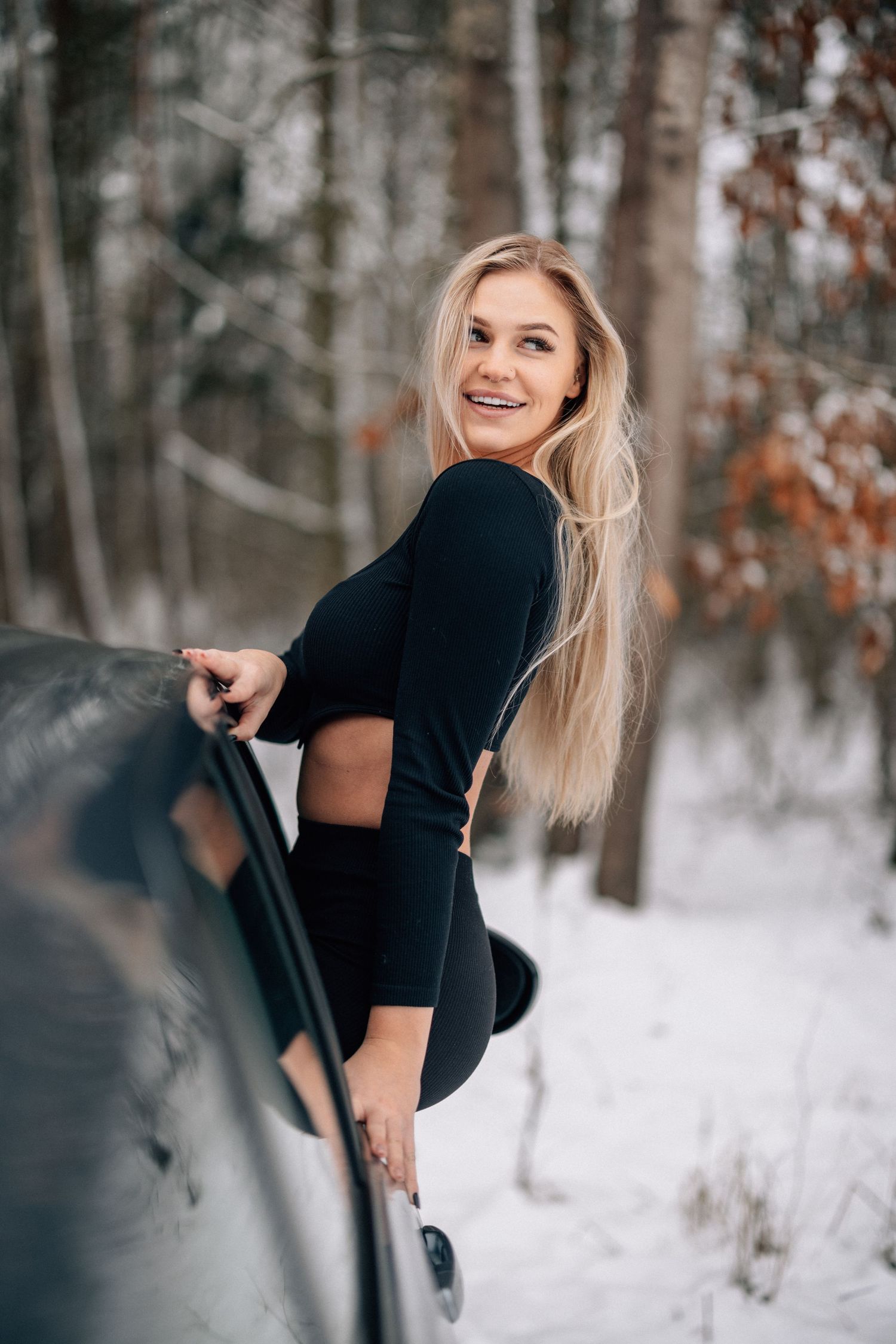 Fashionable winter portrait against a snowy forest backdrop with a parked car.