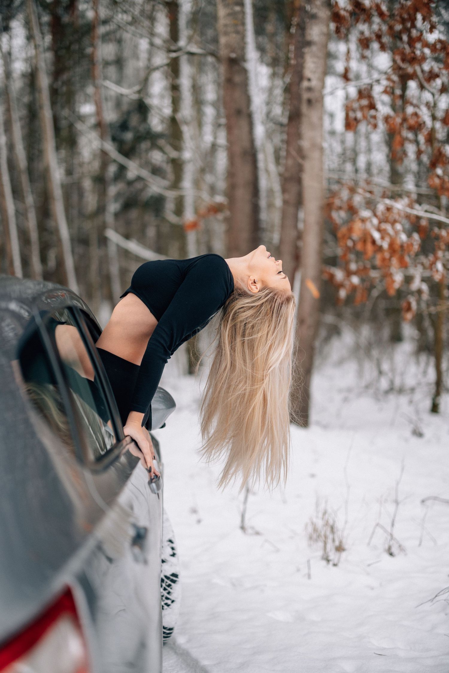 Artistic winter photo of someone playfully leaning out a car window in the snow.