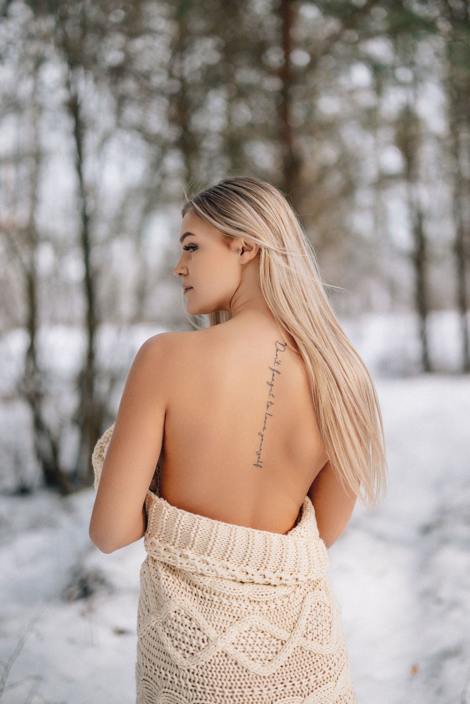 Back view portrait in snowy forest setting with delicate knit sweater and spine tattoo.