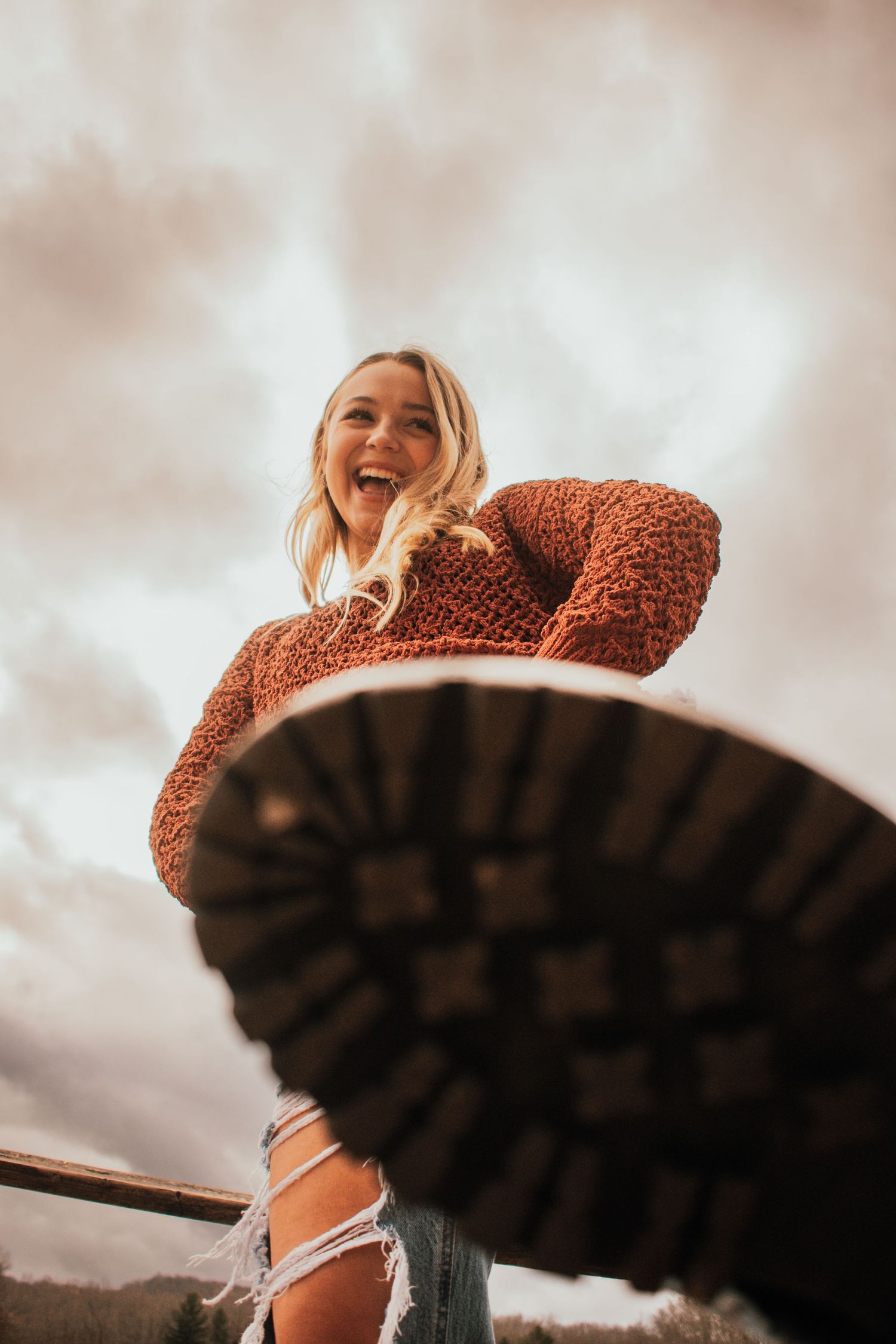 Creative low-angle portrait showing boots and a cozy sweater against a cloudy sky.