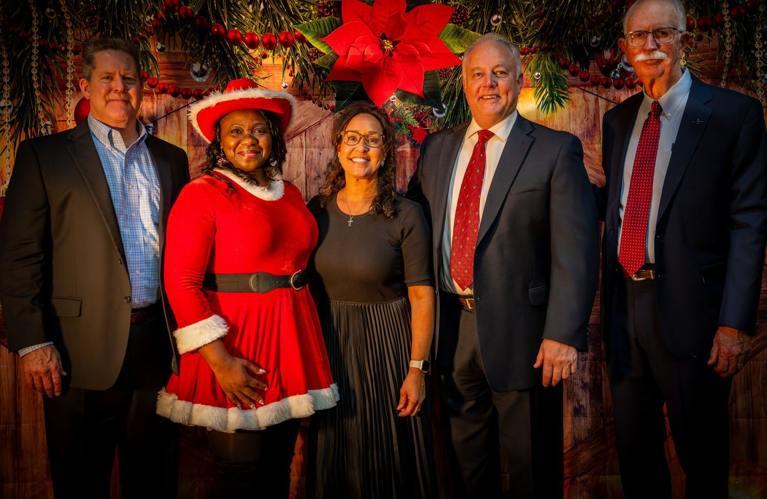 A group photo of people posing together at a holiday party with festive red decorations and greenery.