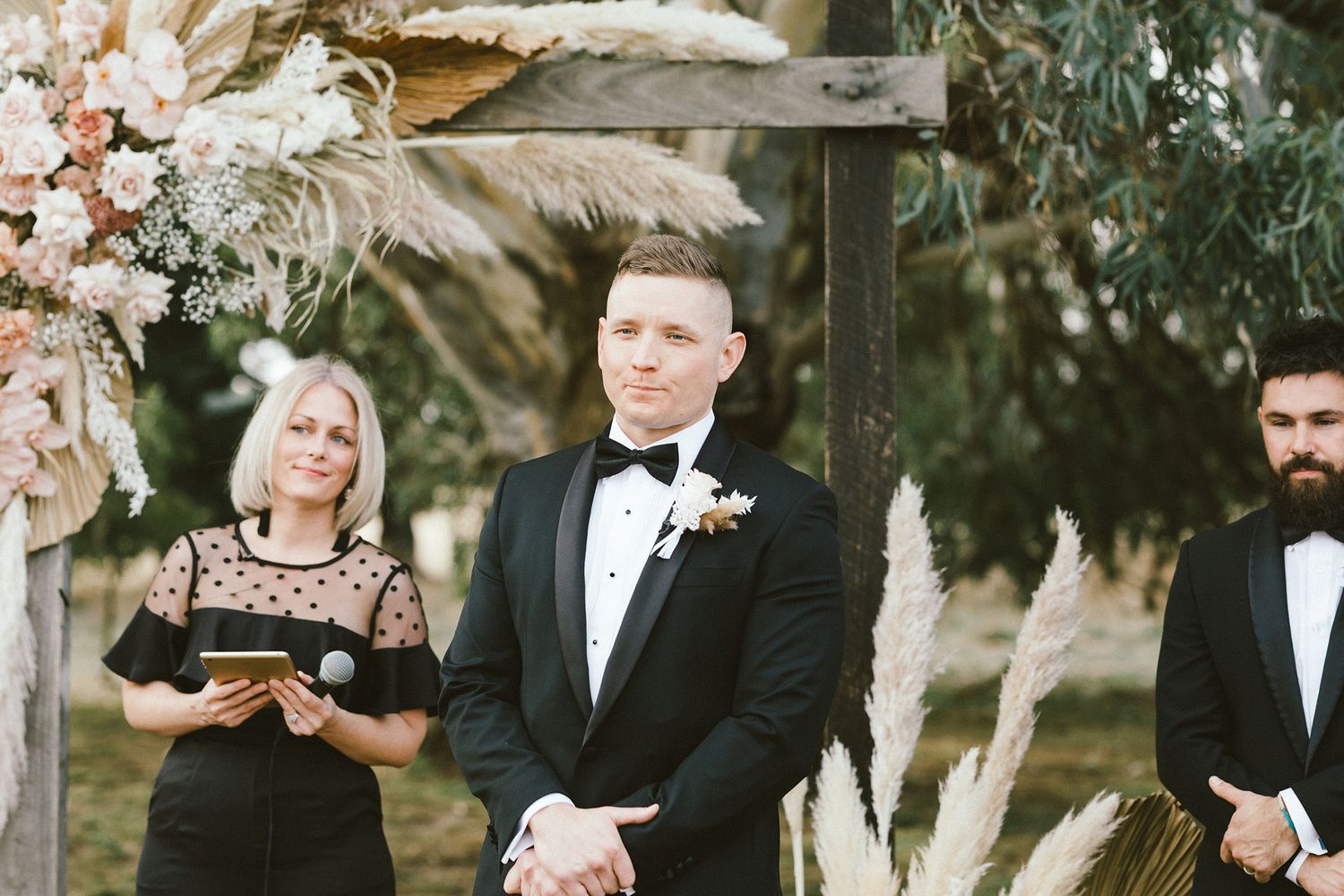 Outdoor wedding ceremony with floral arch and dried pampas grass decorations.