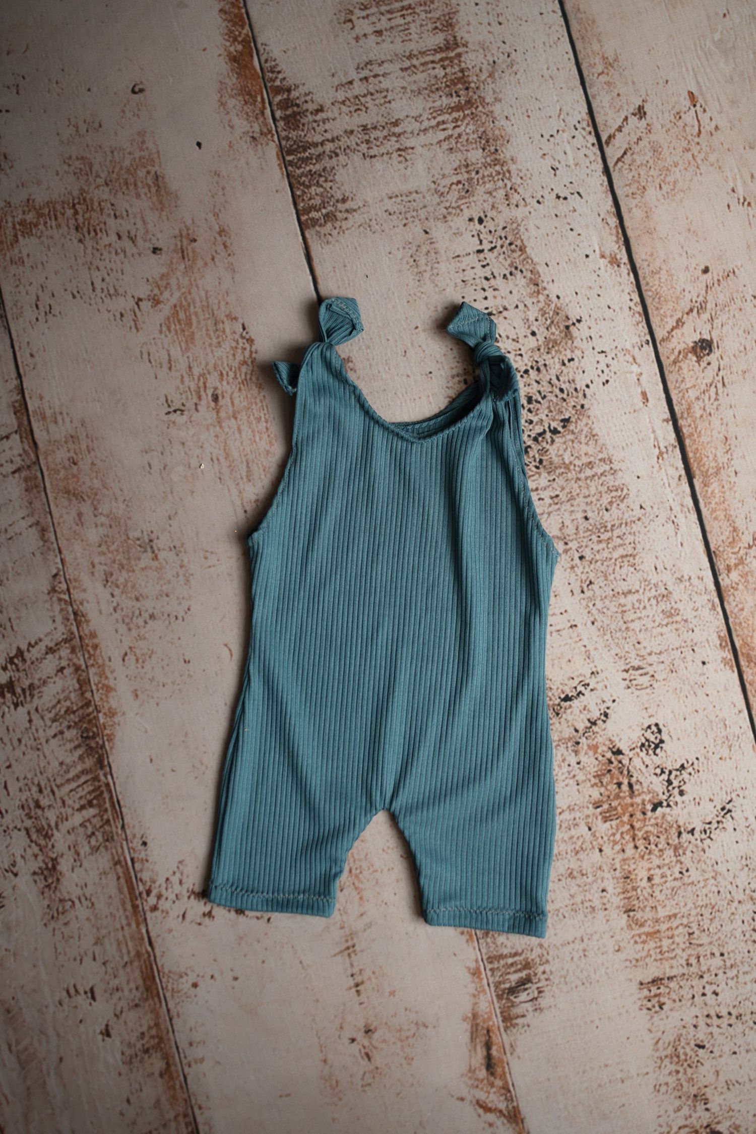 Teal ribbed cotton baby romper displayed on a rustic wooden background.