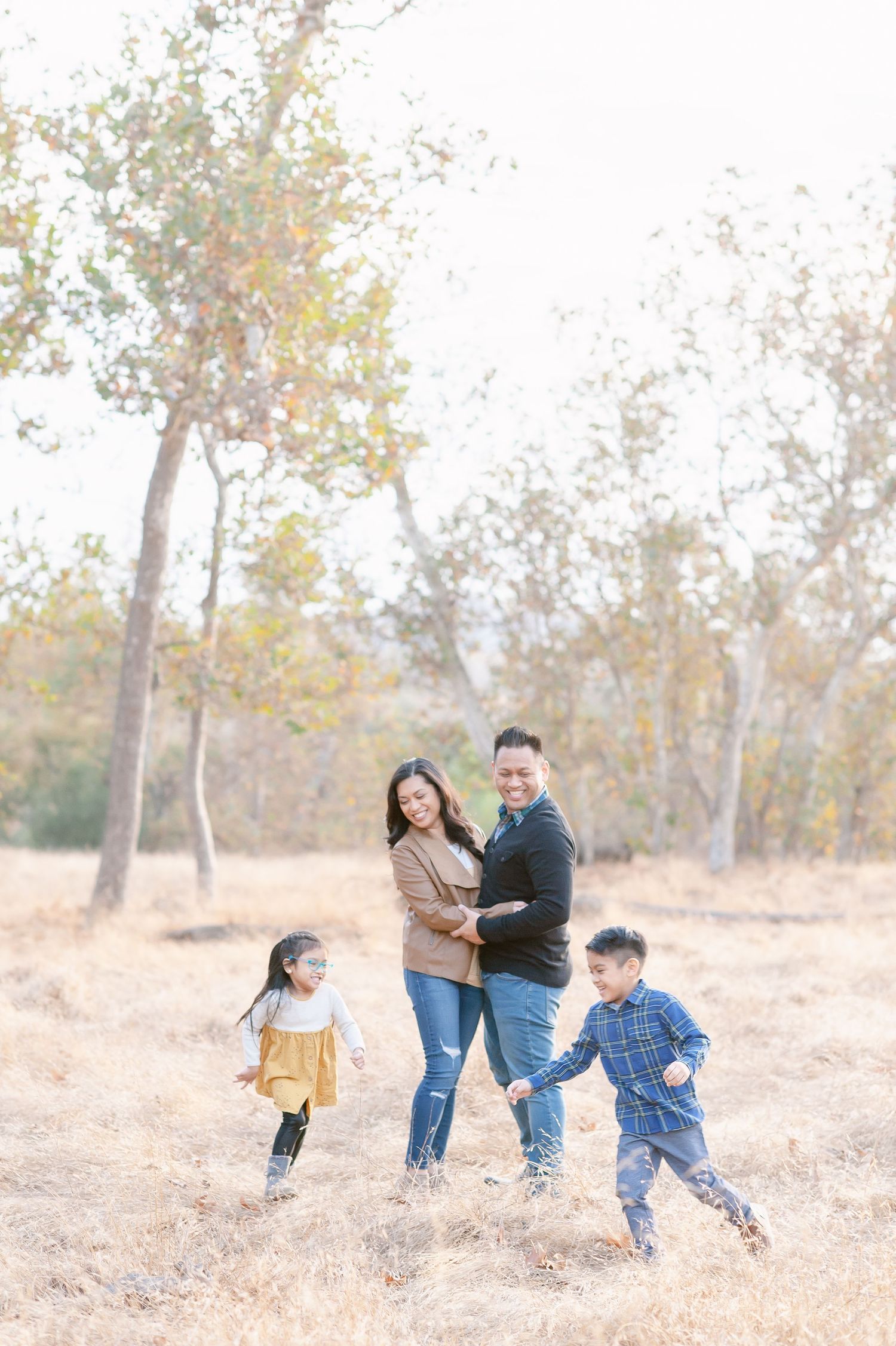 family portrait of mother and father embracing while watching their two childern (a boy and girl) run around them.