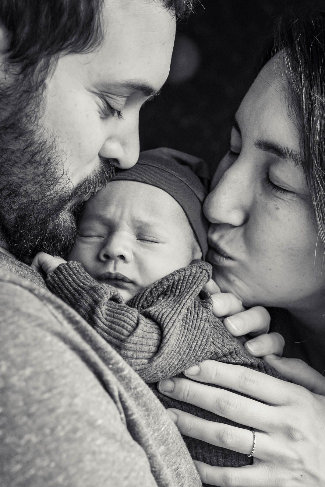 Black and white photo of parents kissing newborn.