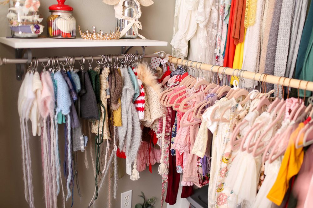 Colorful baby clothing and accessories hanging neatly on closet rods in an organized nursery wardrobe.
