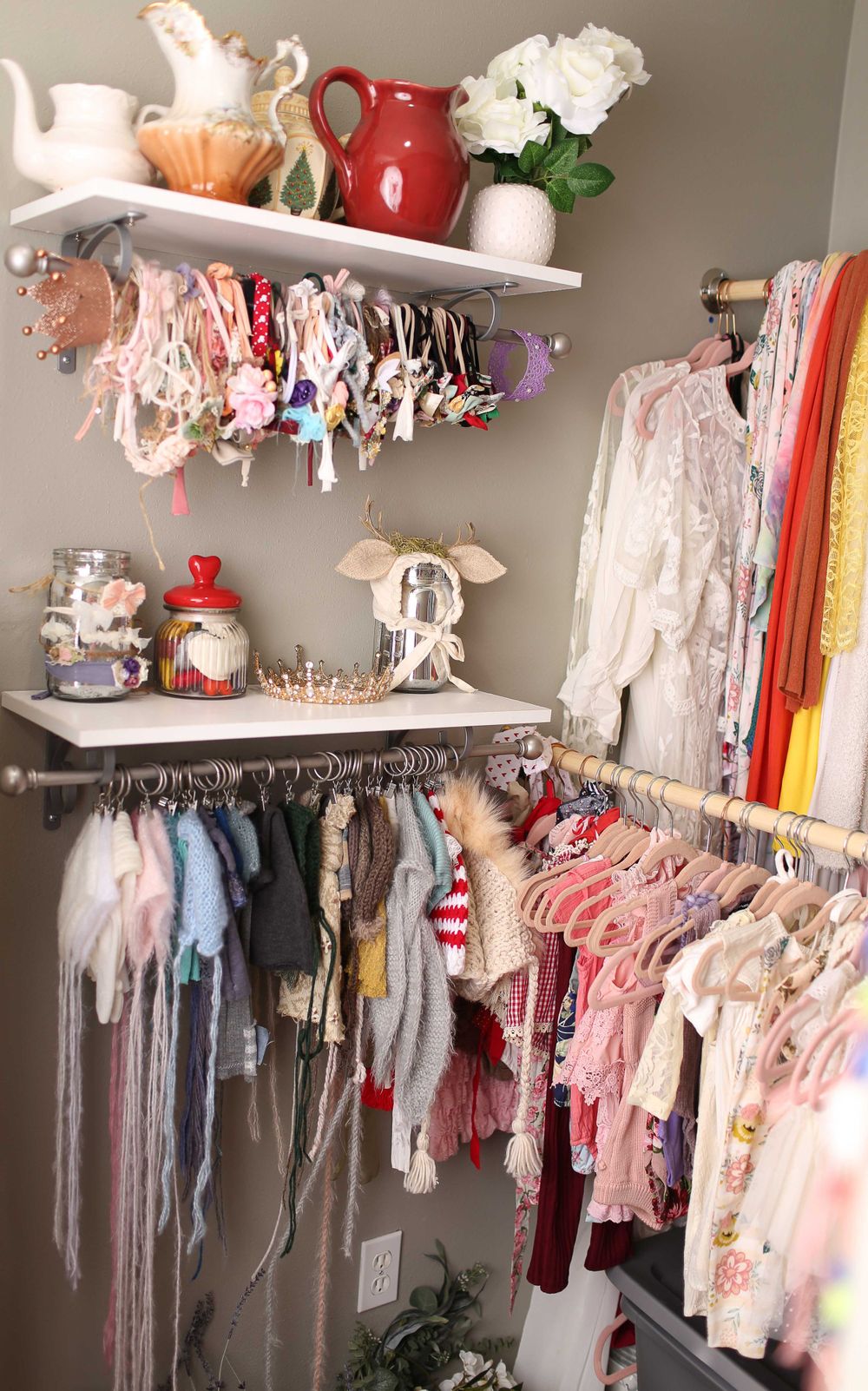 Baby nursery closet with organized clothing racks, white shelving, decorative pitchers and vases on display, and hanging accessories.