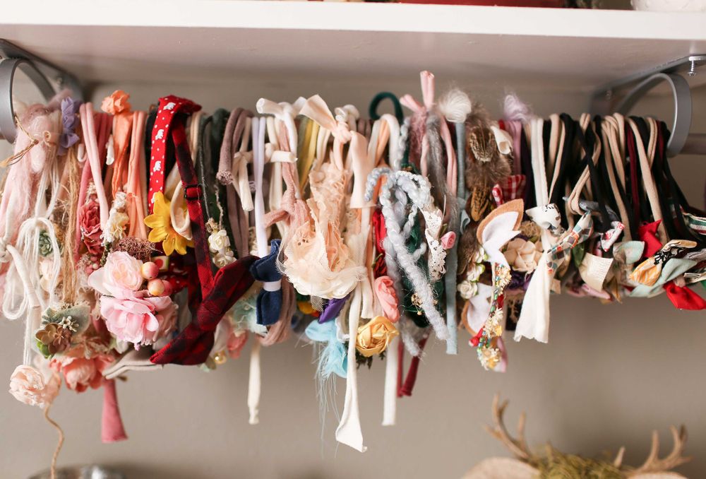 A collection of colorful decorative hair accessories and scrunchies hanging on a closet rod in an organized display.