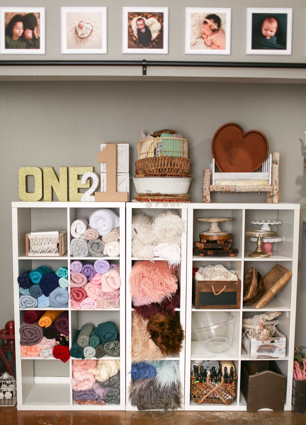 White cube storage unit filled with yarn, crafting supplies, decorative letters spelling 'ONE' and heart decor on shelf.