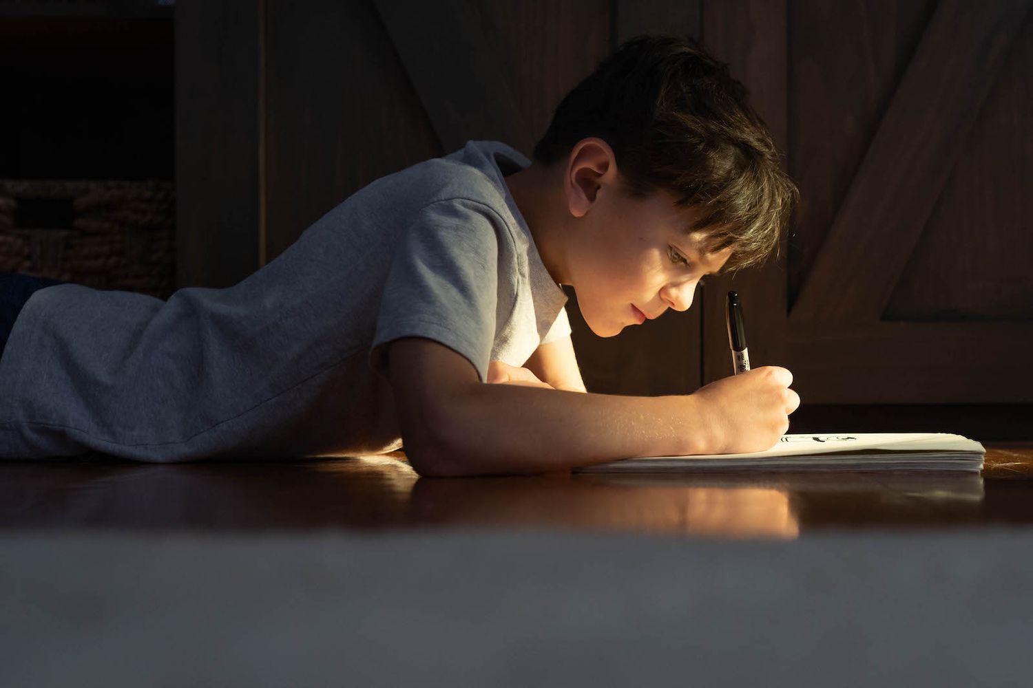 young boy laying on stomach in a pool of light drawing in a sketchpad