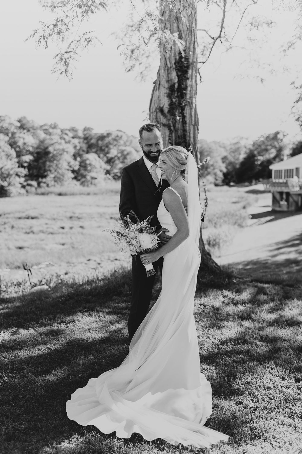 Black and white wedding portrait with a flowing bridal gown and natural outdoor backdrop.