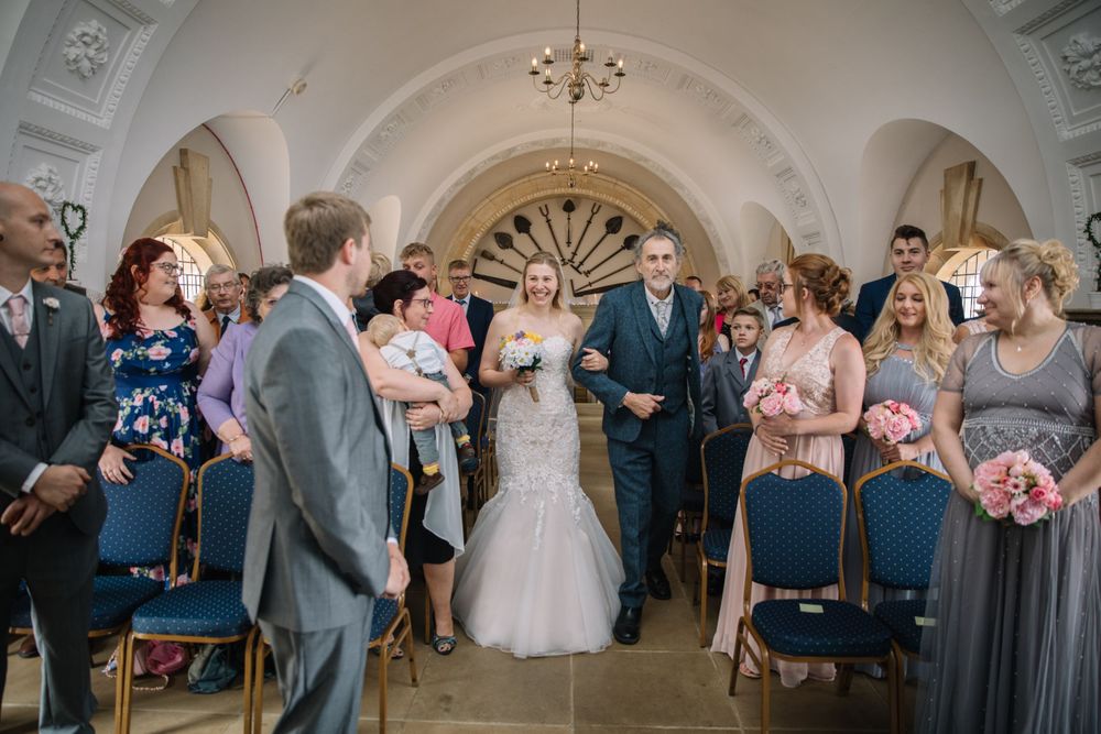 Wedding ceremony procession in an elegant venue with arched ceilings and decorative details.
