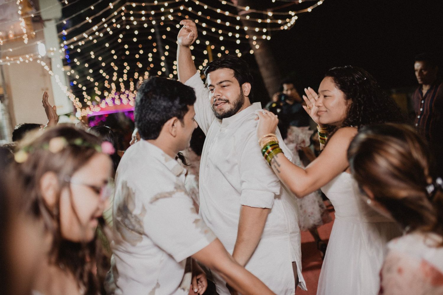 Wedding reception guests dancing and celebrating under twinkling string lights at an evening celebration.