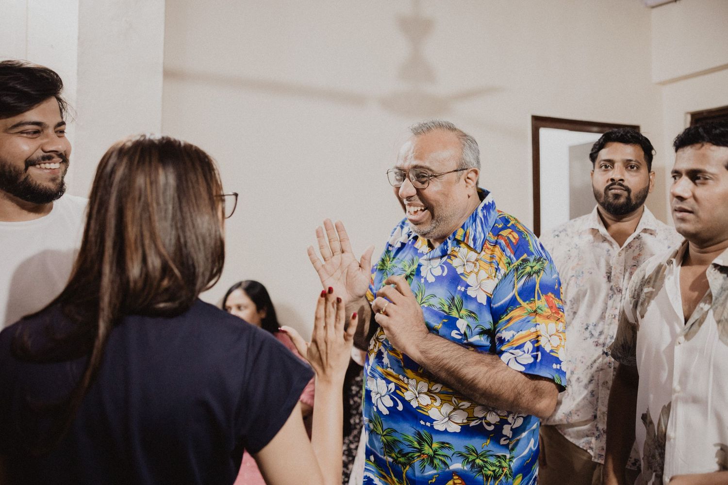 People socializing and laughing together at an indoor gathering with white walls.
