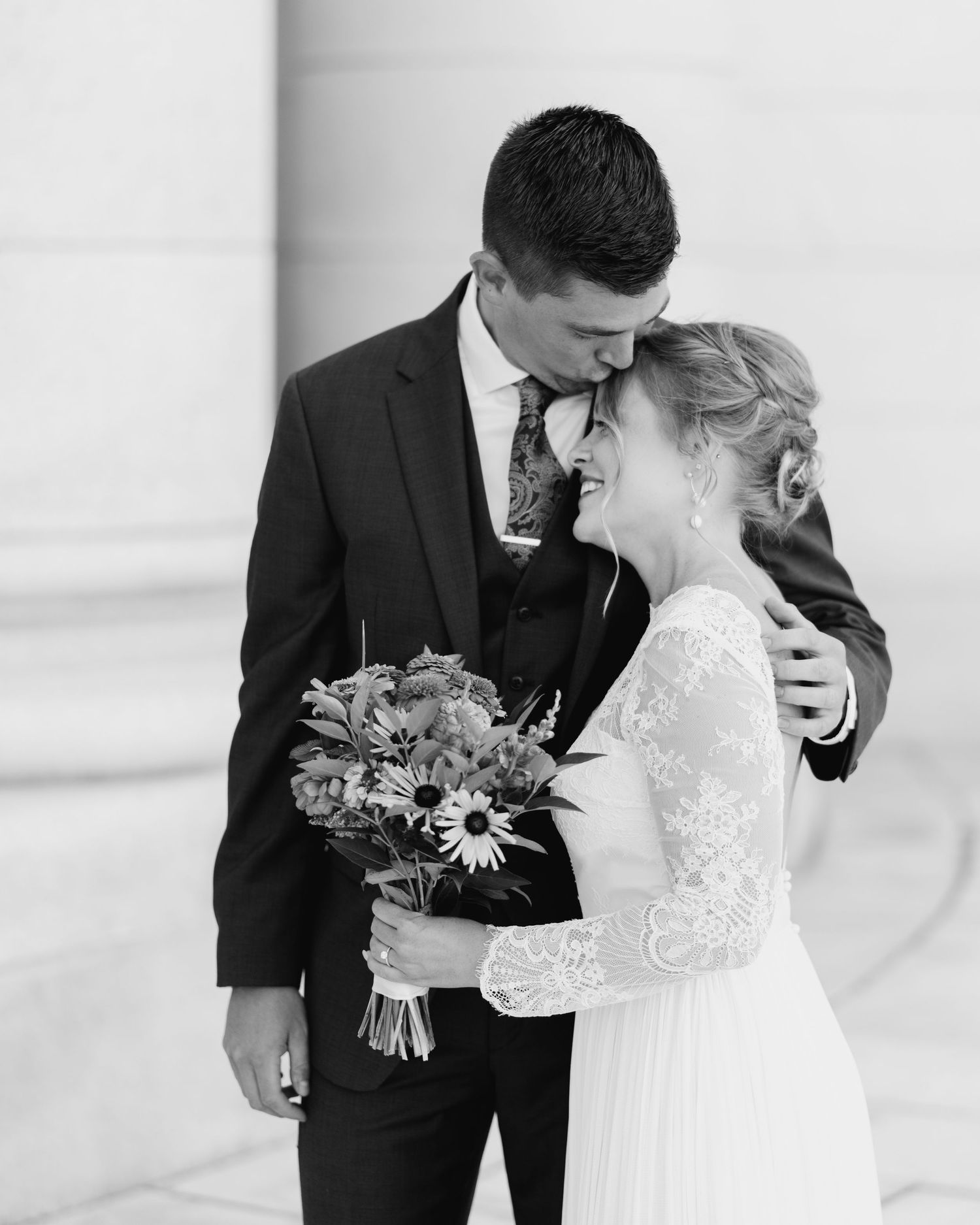 Romantic black and white wedding portrait with couple embracing and holding floral bouquet.