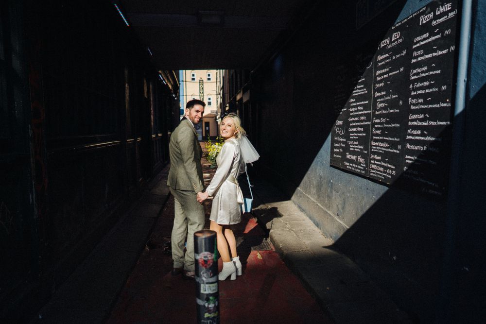 A couple walks hand in hand down a dark corridor with a menu board visible on the wall.