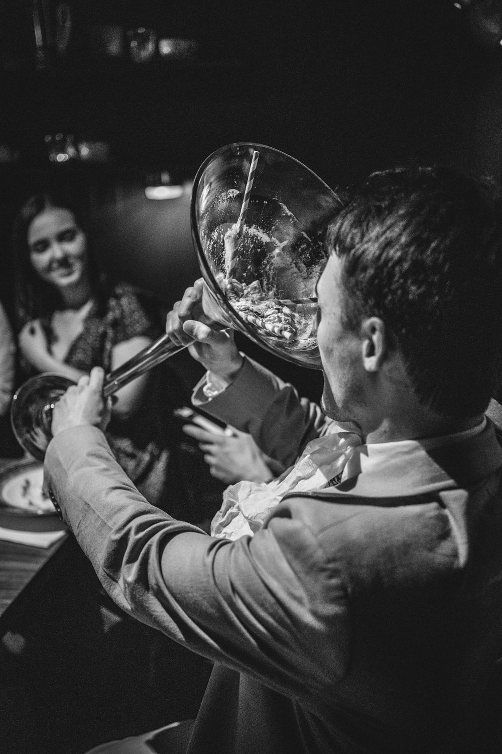 A person raises a large glass for a toast in a moody black and white setting.