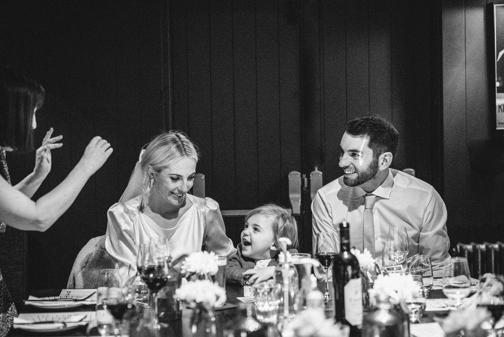 A candid black and white photo of wedding guests laughing during dinner.