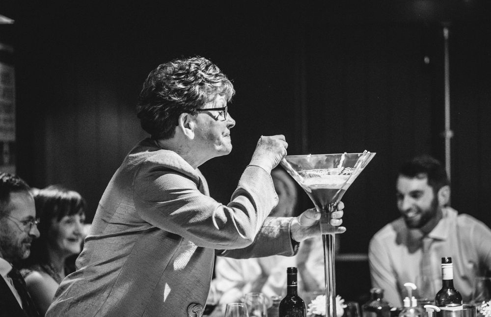A candid black and white photo of someone drinking from a large martini glass at a celebration.