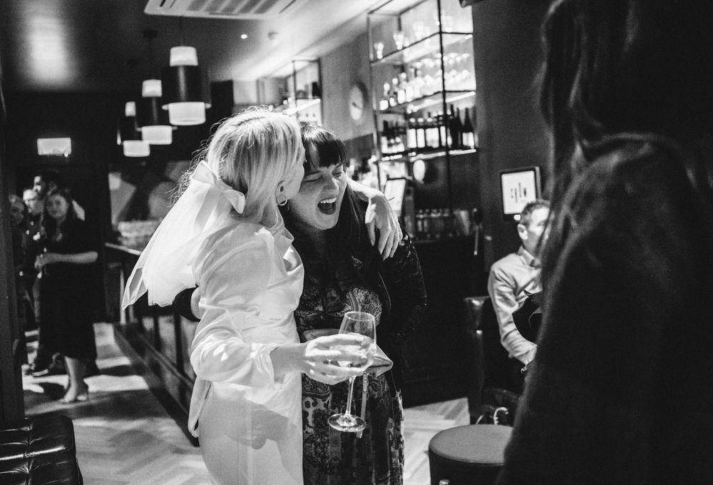 A black and white photo capturing a joyful moment at a wedding reception in a bar setting.