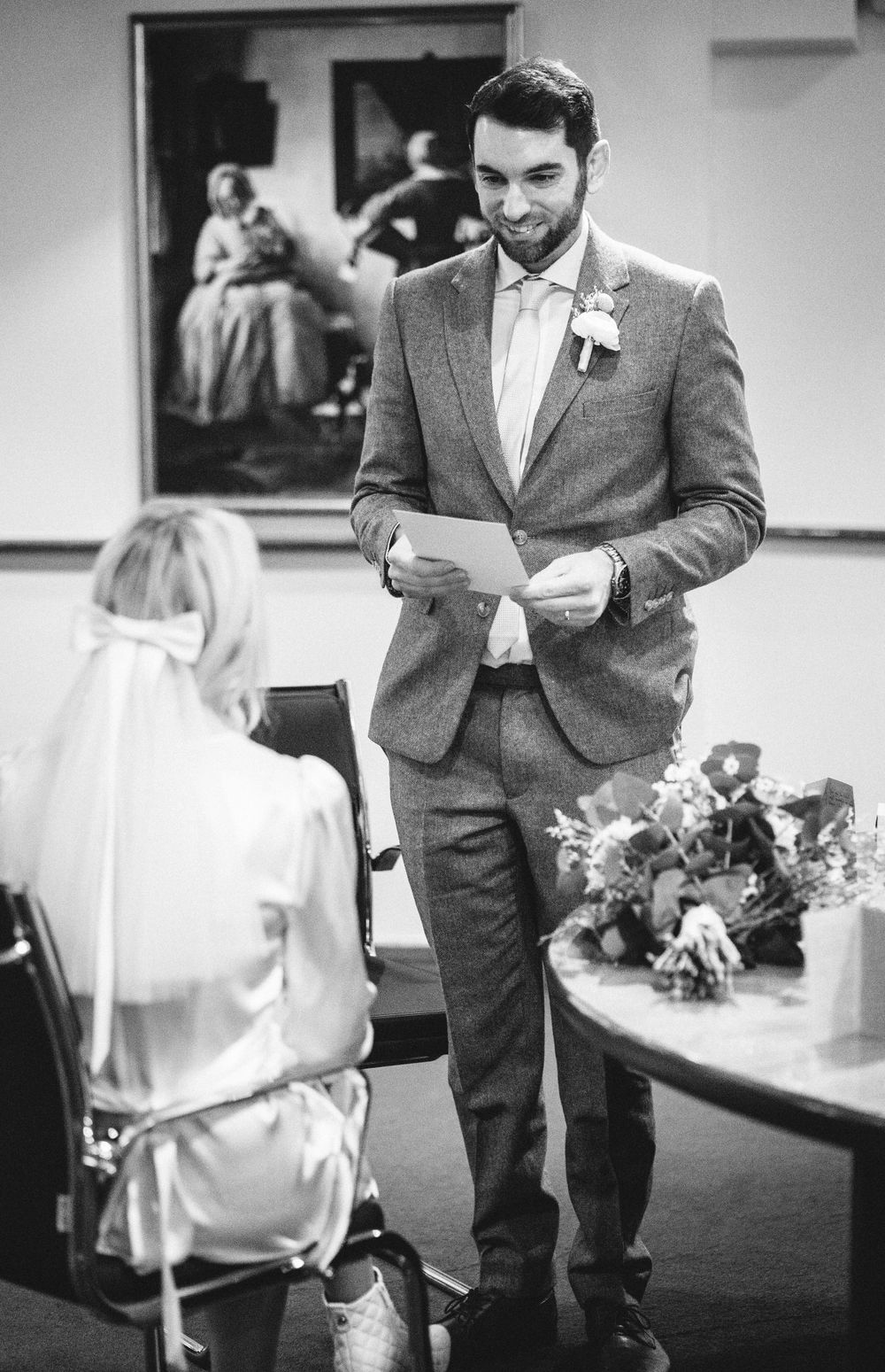 A couple sharing a moment during a wedding ceremony with the groom reading a note in a gray suit.