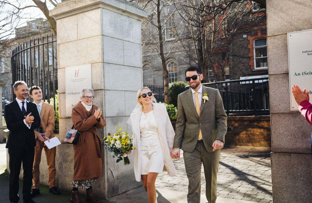A couple exits through stone pillars while guests look on during their wedding day.