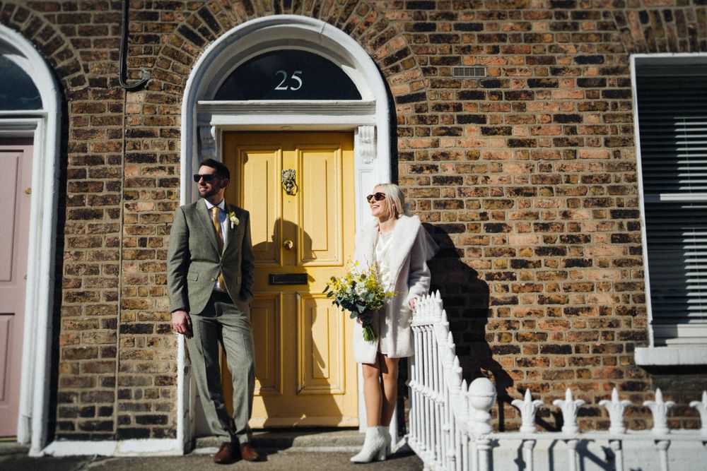Well-dressed pair stands on brick building steps with yellow door numbered 25.