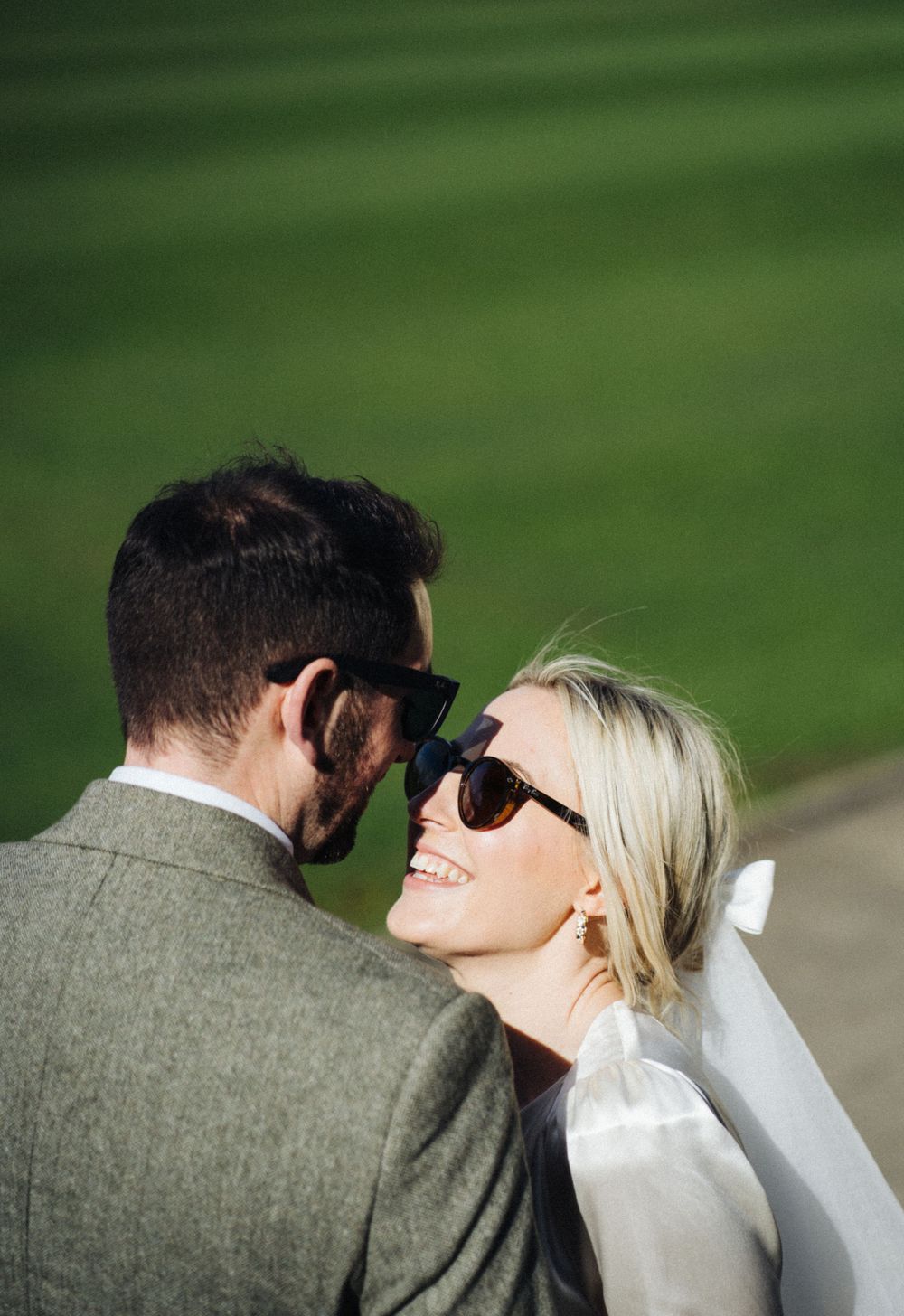 A couple wearing sunglasses shares a joyful moment in front of a green background.