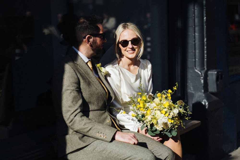 A couple sits together holding yellow flowers in dramatic lighting.