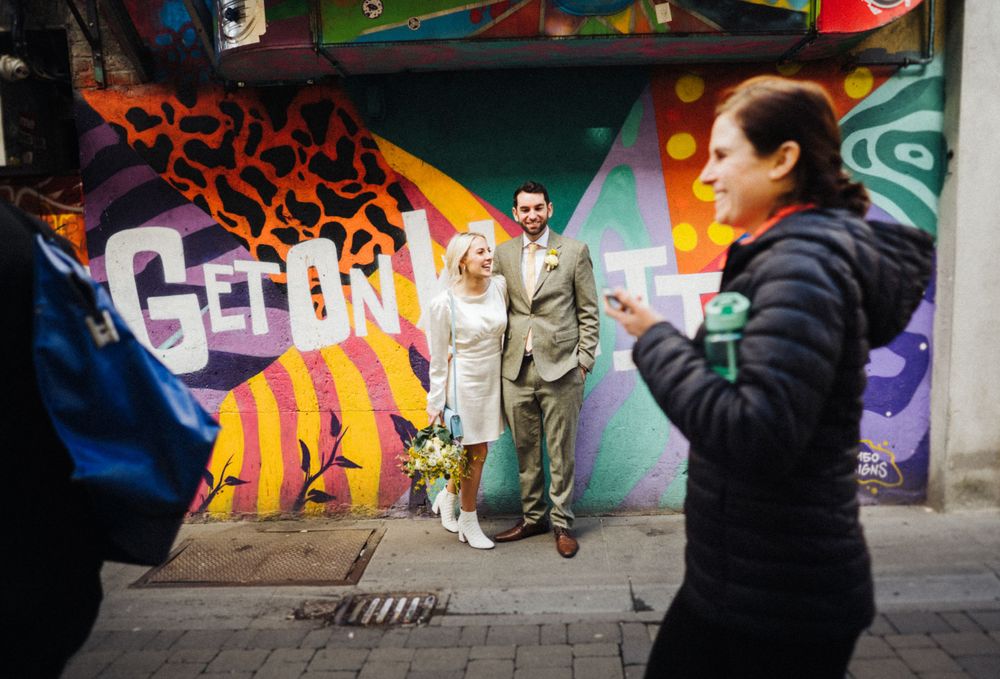 A couple poses in front of vibrant street art and graffiti on an urban wall.