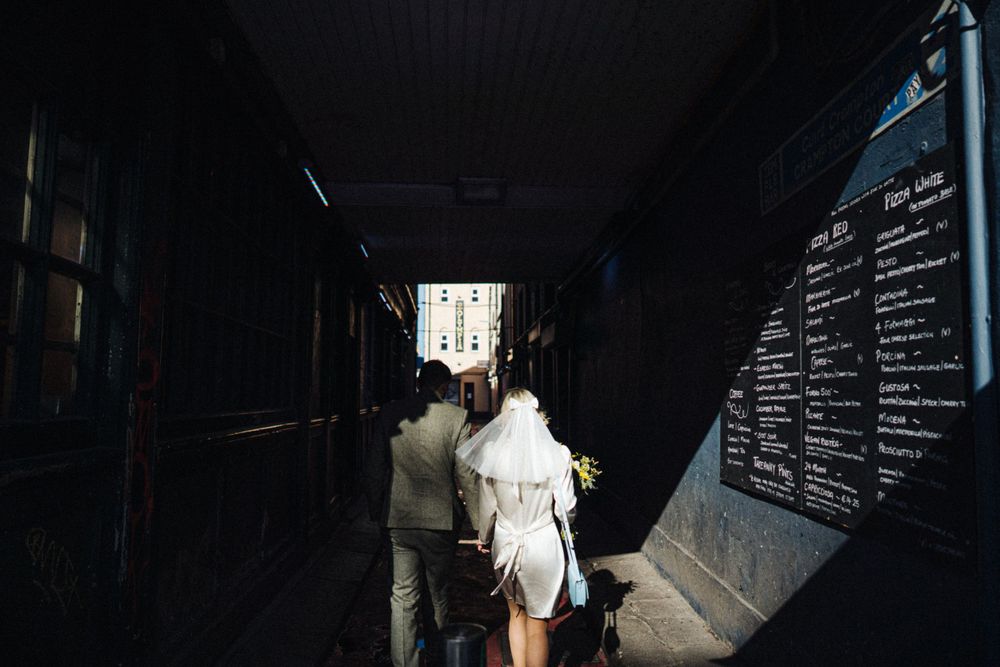 A couple walks through a dark tunnel with a menu board visible on the wall.