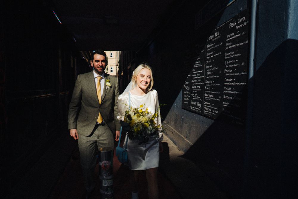 A couple emerges from a dark passageway carrying yellow flowers.