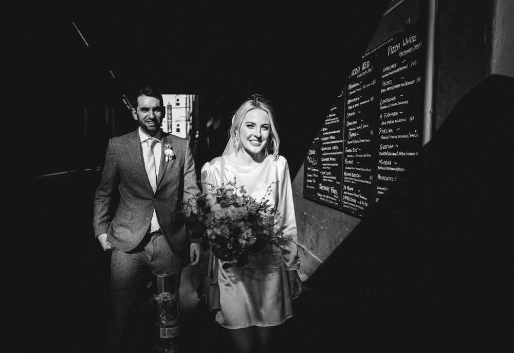 A black and white photo of a couple walking through an alley with text on the wall.