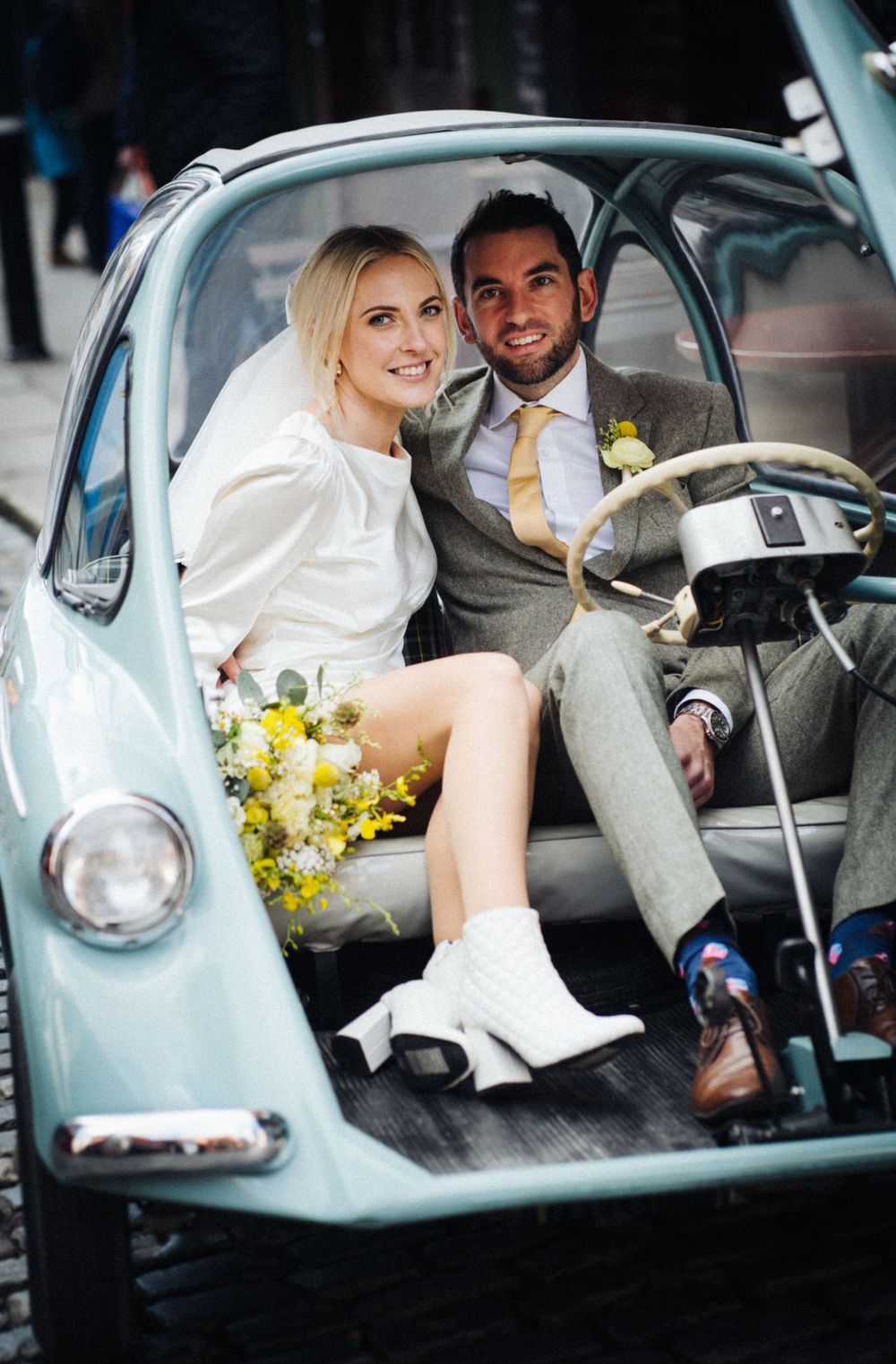 A couple sits in a vintage light blue car with yellow flowers on the dashboard.