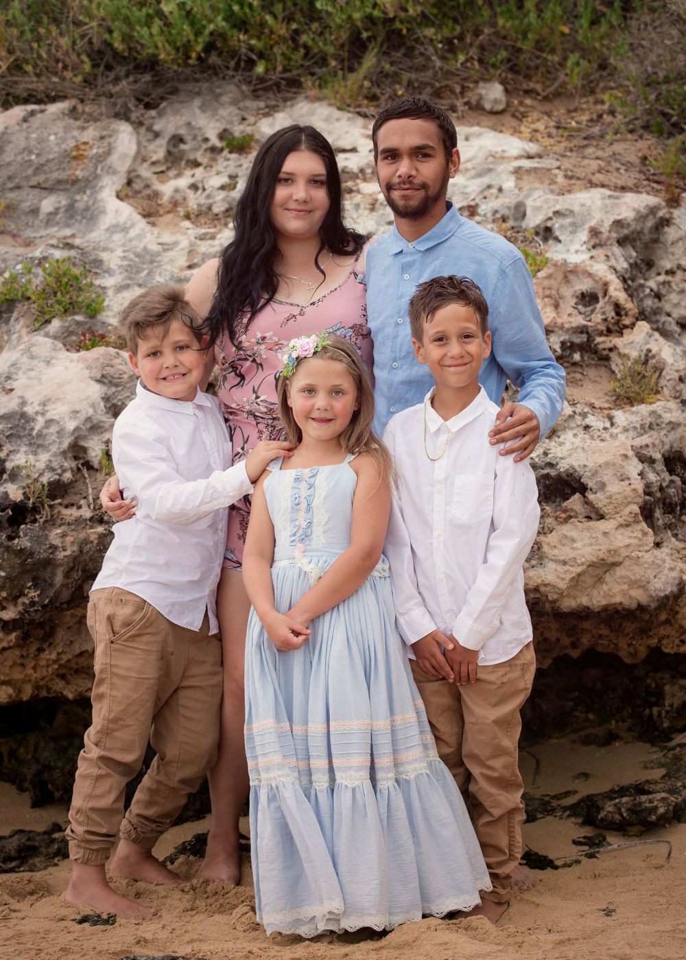 Family of 2 boys, a girl and their parents at the beach in front of sandstone boulders at Point Peron Rockingham.