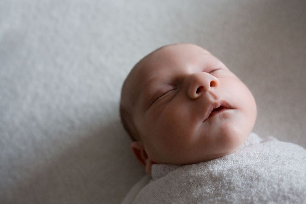 A sleeping newborn rests on white fabric in soft window light.