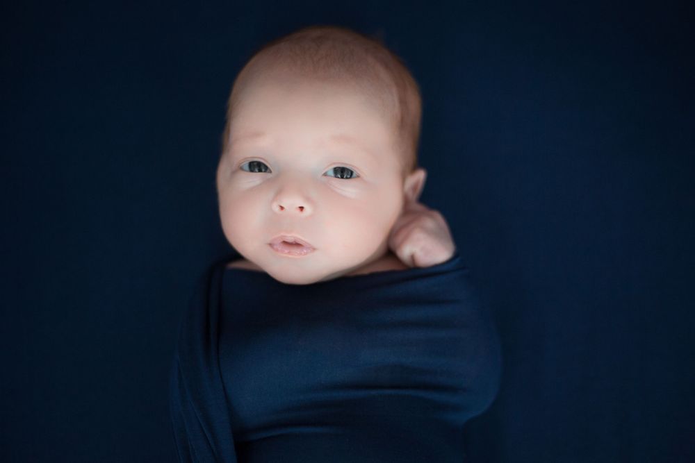 A peaceful baby wrapped in dark blue fabric against a navy background.
