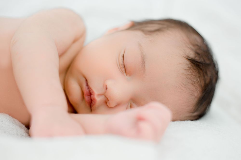 A peaceful newborn sleeps on soft white bedding in natural light.