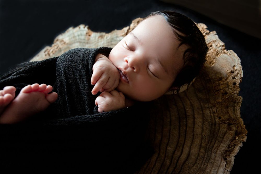 A sleeping baby in black clothing rests on a rustic wooden surface.
