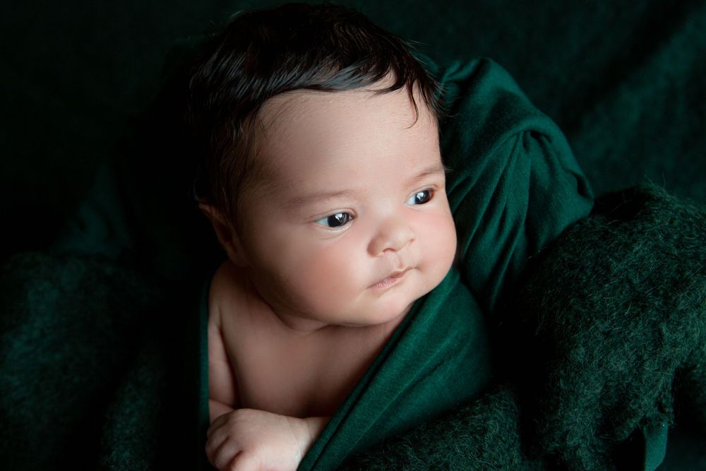 A bright-eyed baby nestled in emerald green velvet fabric.