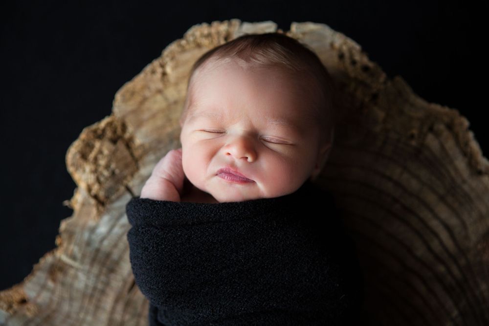 A peaceful sleeping newborn wrapped in black fabric on wooden texture.