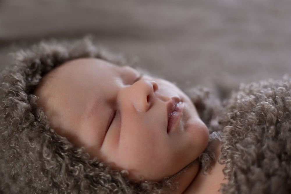 A peaceful infant sleeps while nestled in soft gray textured fabric.