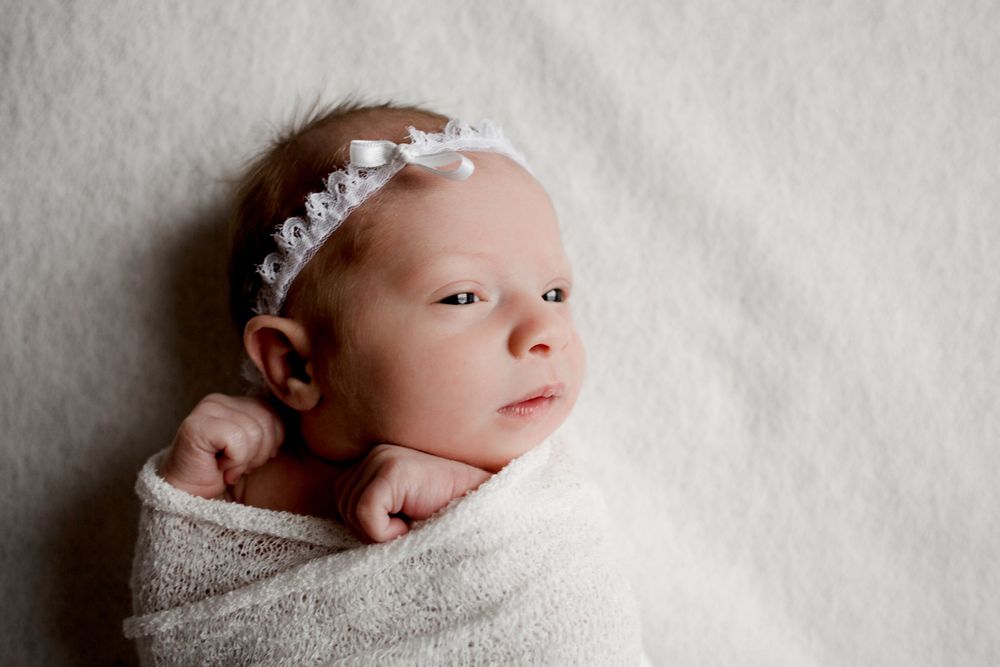 A newborn baby wearing a delicate lace headband wrapped in soft beige fabric.