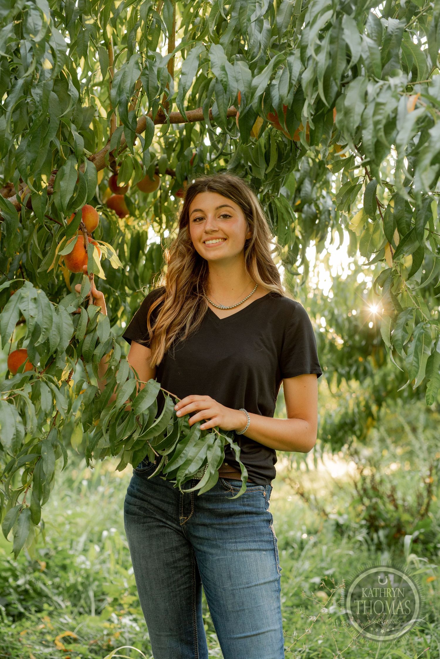 Casual portrait among peach trees with golden sunlight filtering through the leaves.