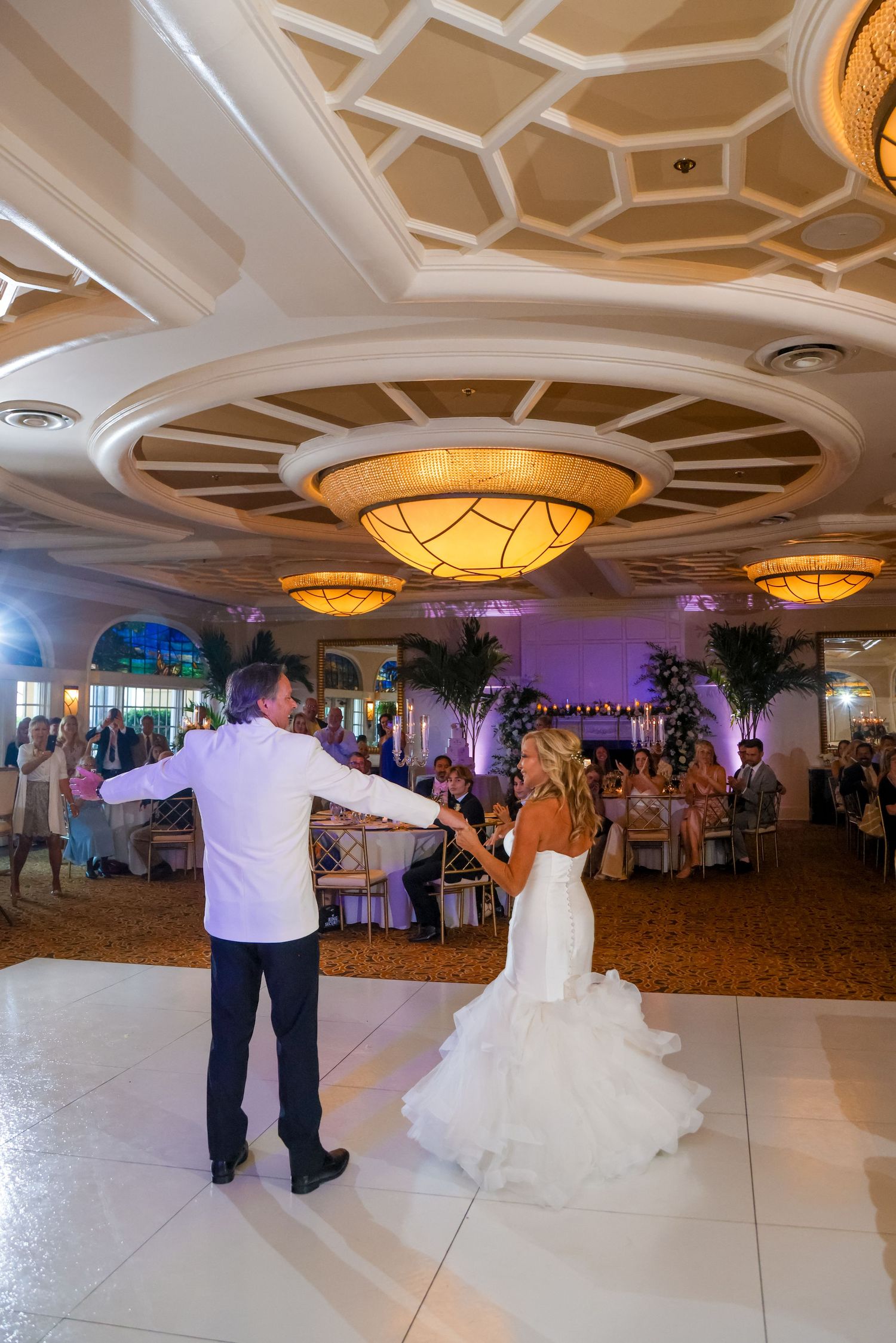 Elegant ballroom reception with ornate ceiling and couple dancing on white floor.