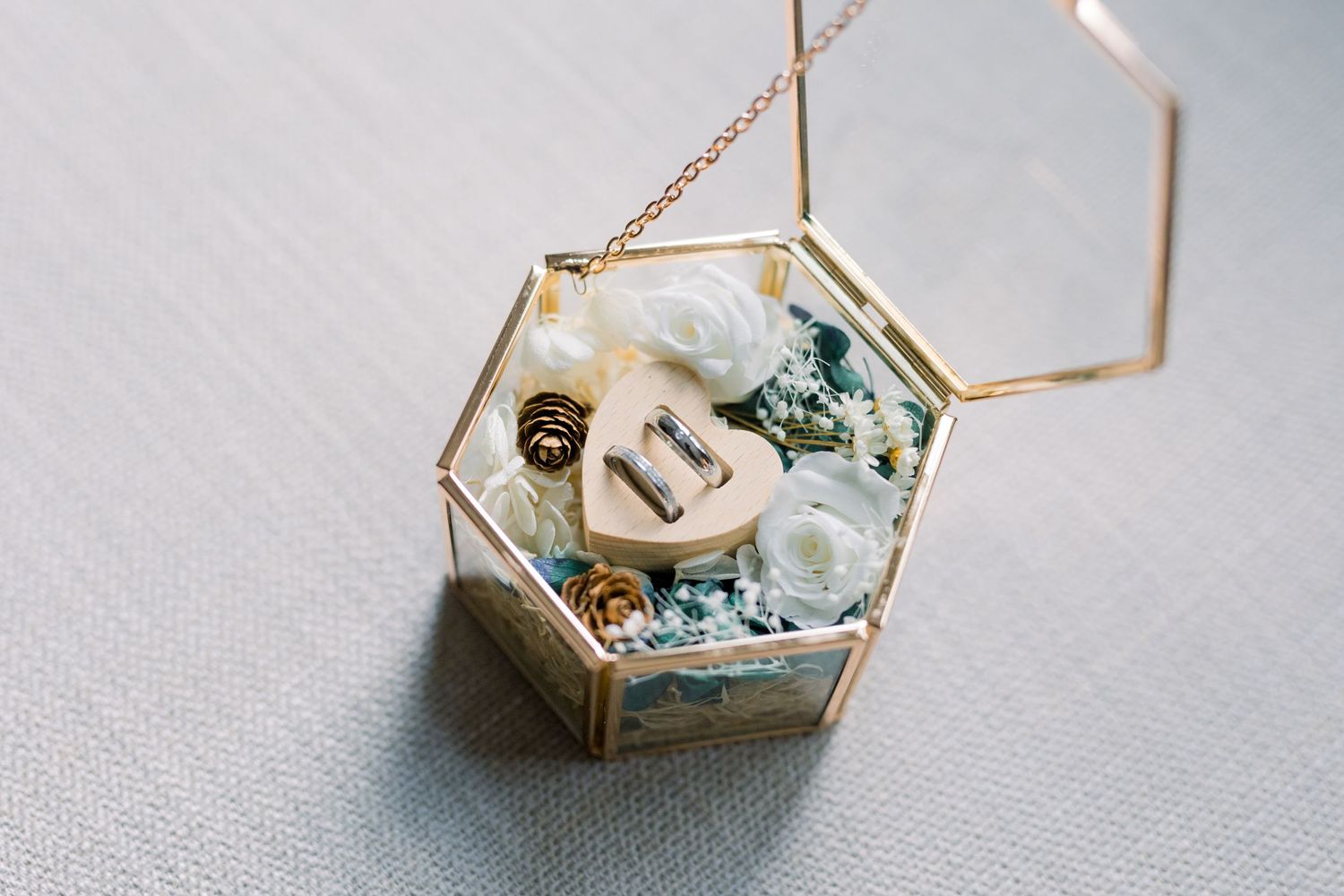 Delicate geometric glass ring boxes with floral designs displayed on gray fabric.