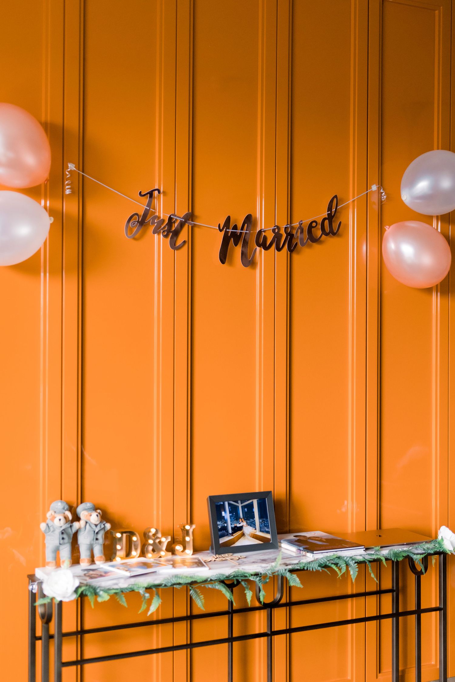 Orange wall decorated with white balloons and text decorations for a celebration.